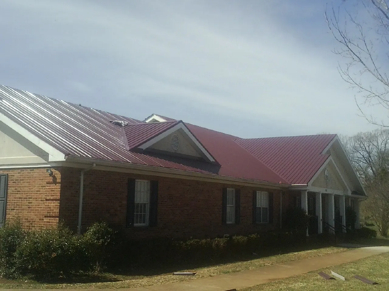 Red metal roof with gabled entries on a long brick building, from a Hail Damage Roof Repair job in Hudson